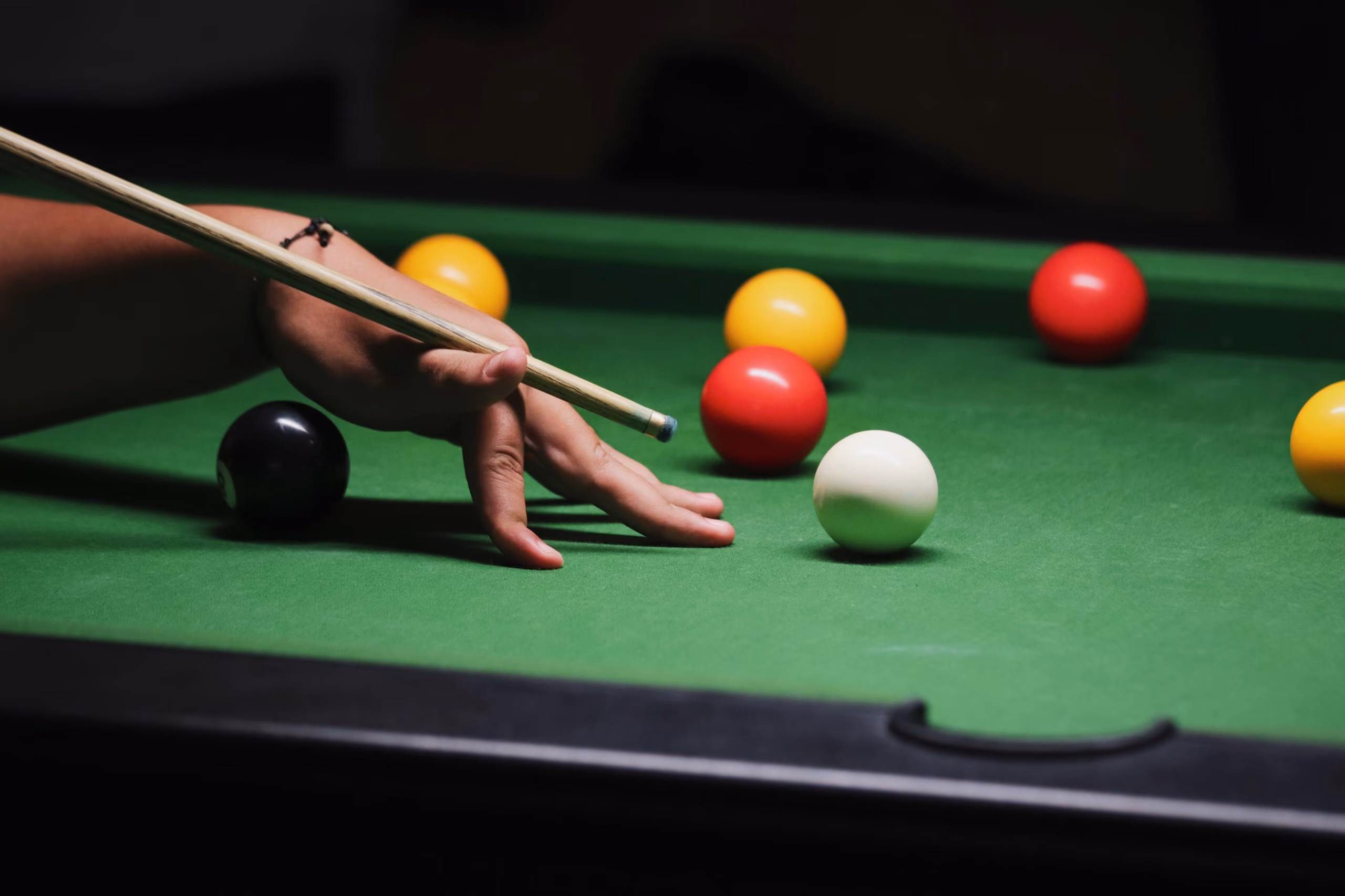 A bridge hand on green cloth, the cue resting across the knuckles, red and yellow balls beyond the white.