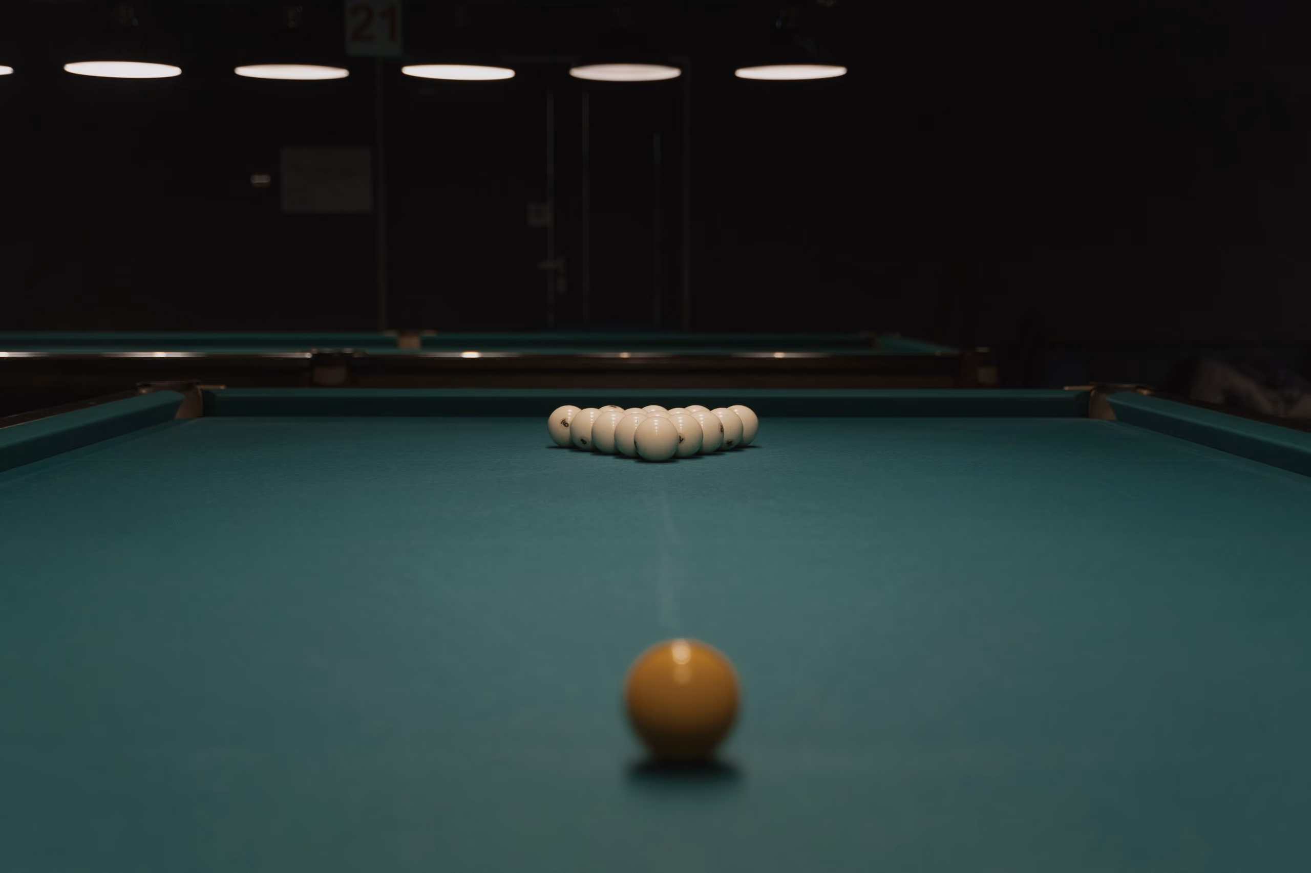 A green table seen from the baulk end, a line of balls racked on the far spot and one ball waiting near the camera.