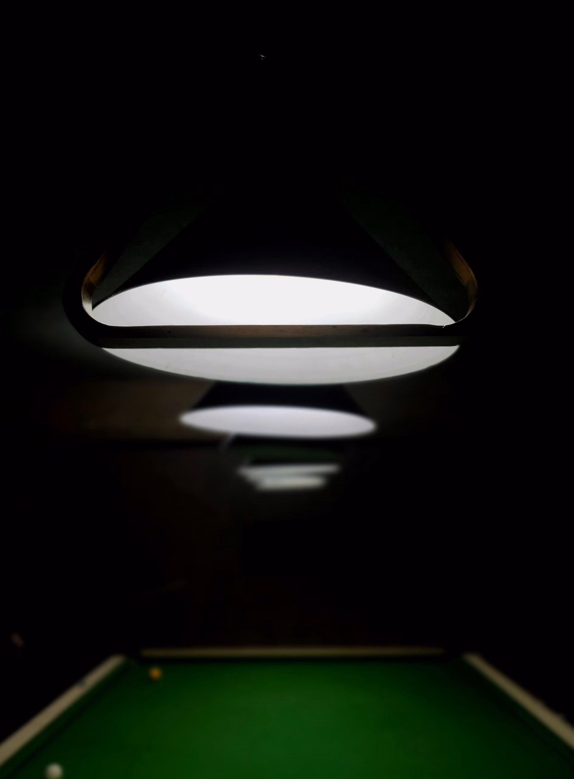 A dark lamp shade seen from below, its white light falling on the green cloth at the bottom of the frame.