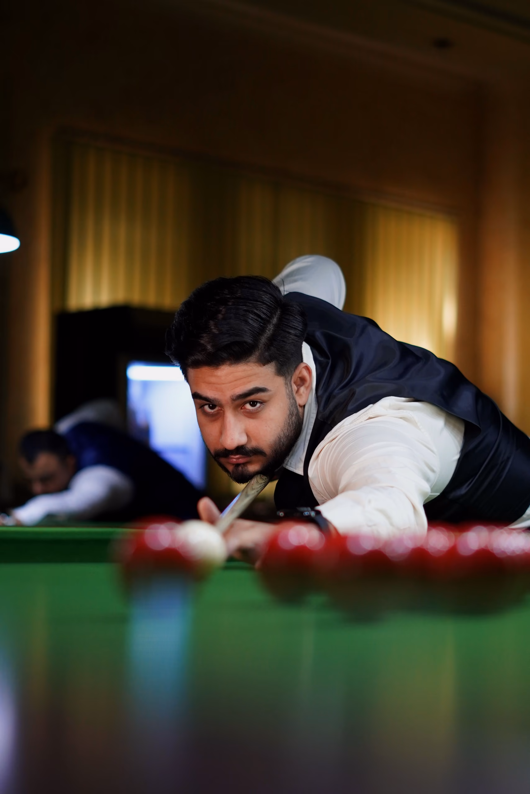 A player in a waistcoat sighting along the cue over a line of red balls on green cloth.