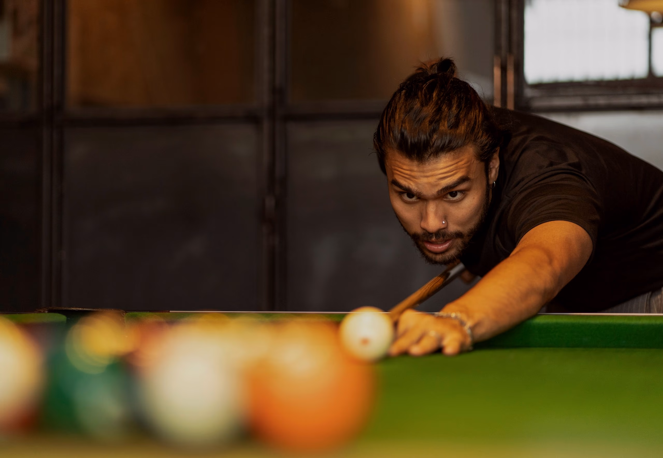 A player down on the cue with his eyes on the shot, coloured balls blurred in the foreground of a green table.