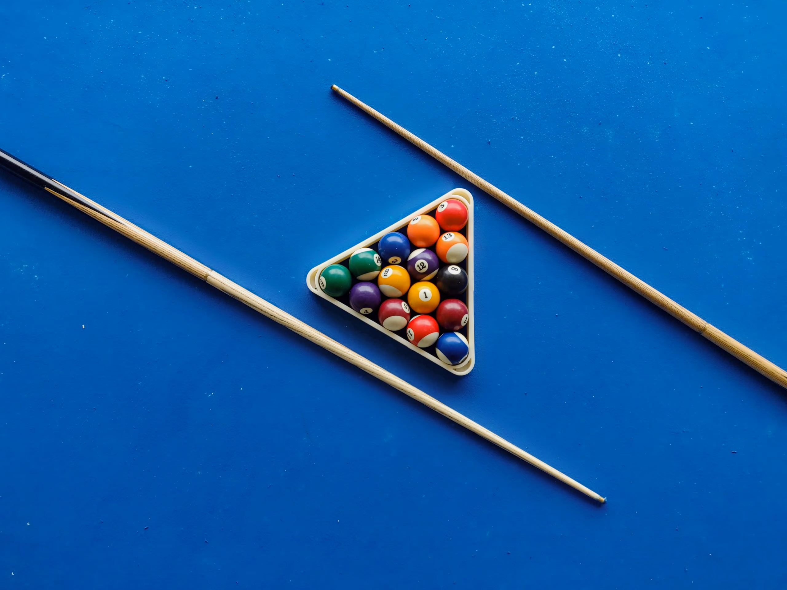 A racked triangle of balls and two cues laid on bright blue cloth, seen from directly above.